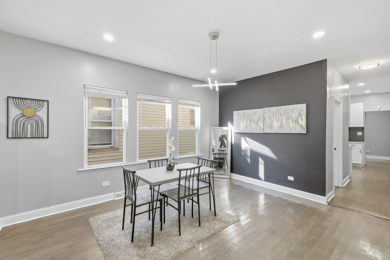 Staged dining room with a table beneath three windows and a charcoal accent wall.