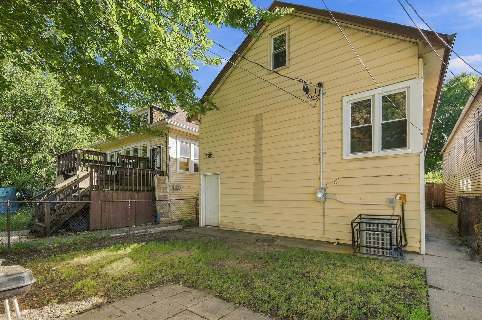 Rear exterior of a yellow-sided house with a raised wooden deck and fenced yard.