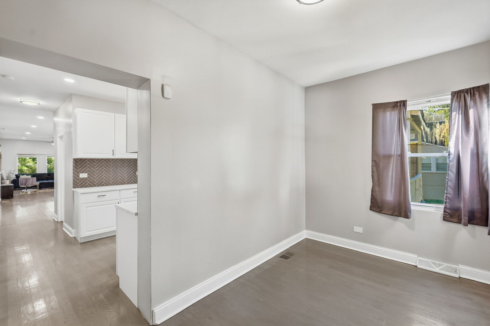 Dining area with gray flooring and a window, opening to the kitchen and living room.