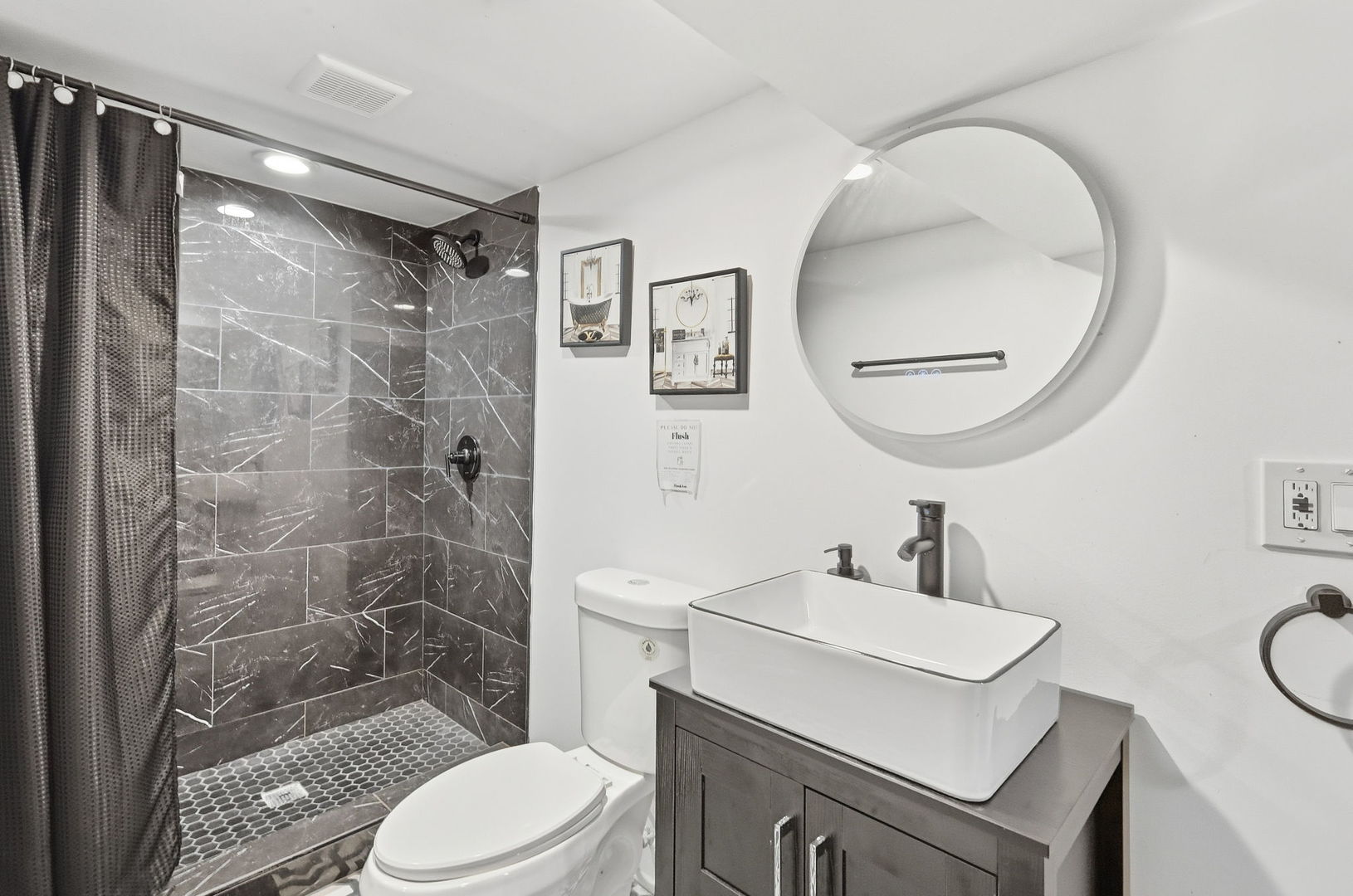 Bathroom with a dark marble-tiled walk-in shower and vessel sink beneath a round mirror.