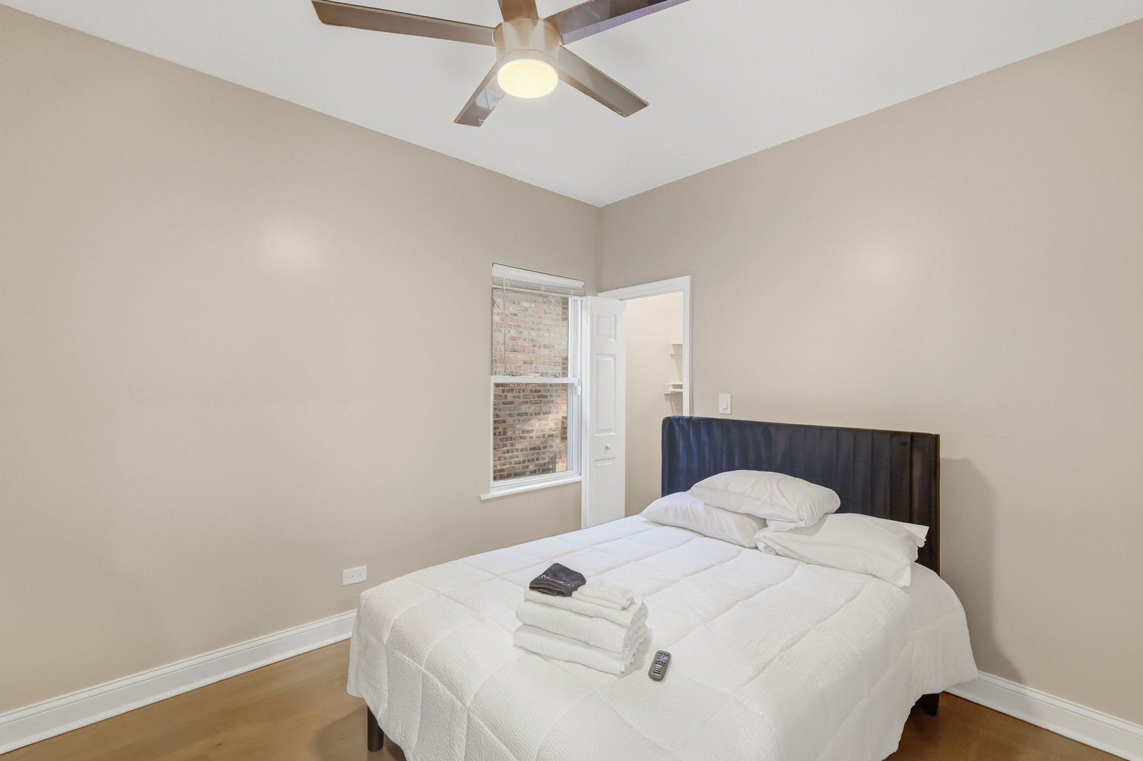 Bedroom with a white bed, dark upholstered headboard, and ceiling fan.