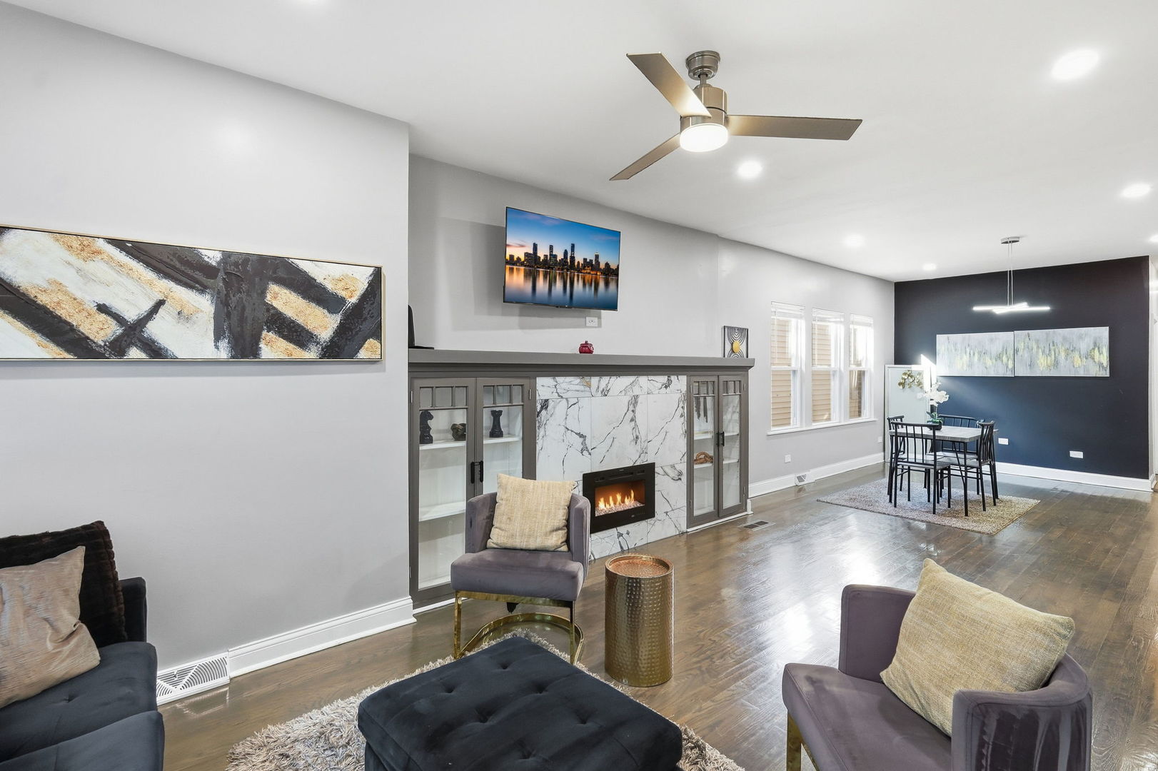 Staged living room with a marble fireplace, gray seating, and an adjoining dining area.