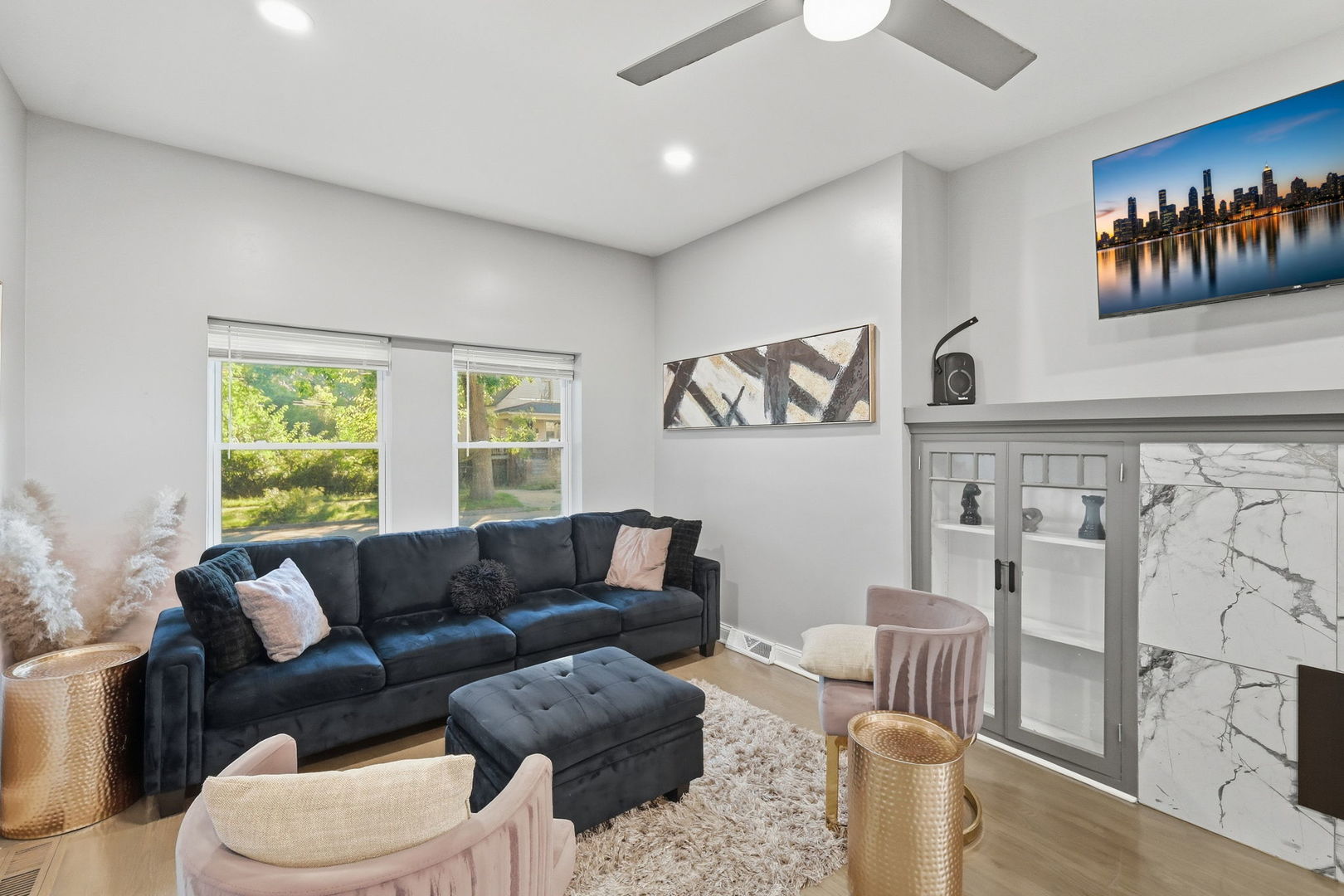 Furnished living room with a dark sectional, pink chairs, and a marble fireplace.