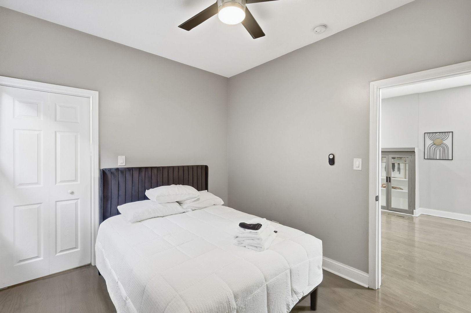 Bedroom with a white bed, dark upholstered headboard, and ceiling fan.