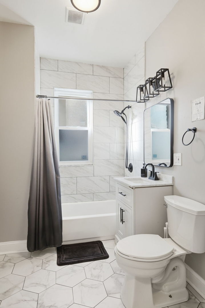 Bathroom with marble-look tile, a tub and shower, white vanity, and hexagonal floor tiles.