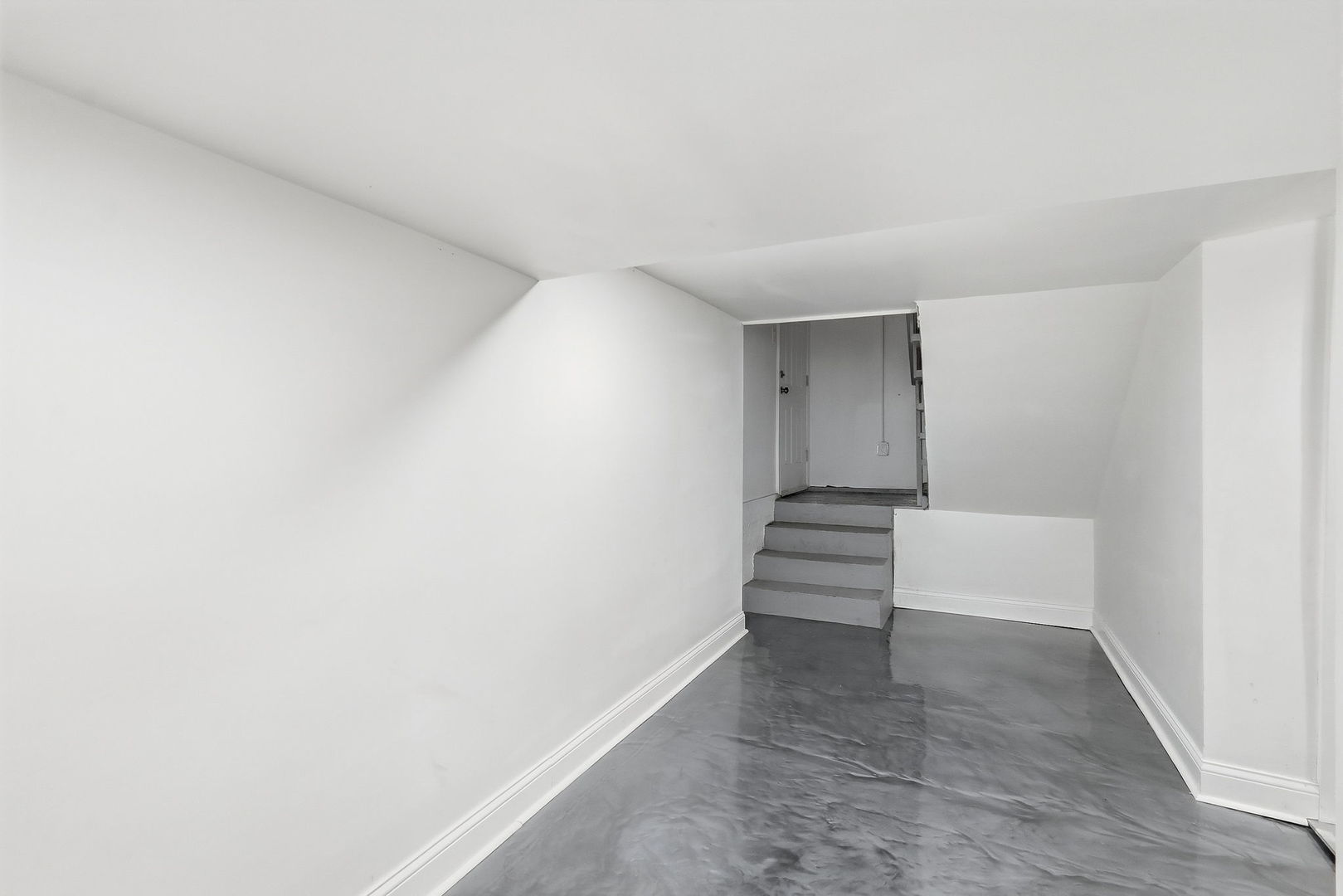 Unfurnished basement room with gray flooring and steps leading to a doorway.