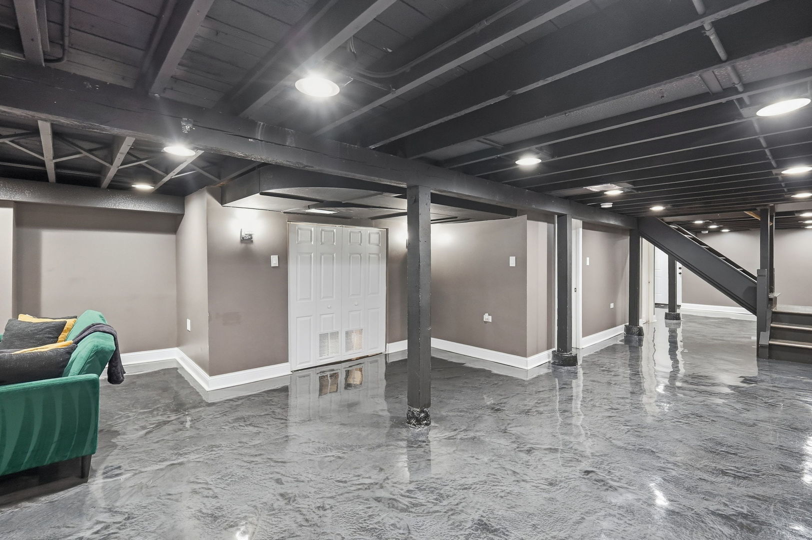 Finished basement with polished concrete flooring, exposed beams, and a staircase.