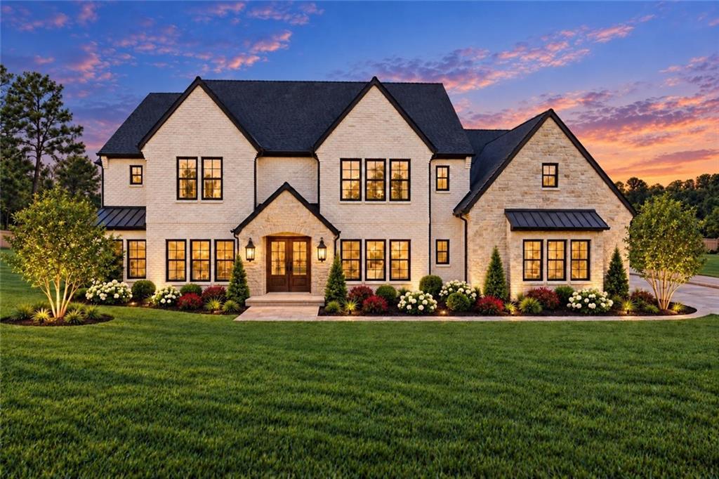 Two-story stone house with a landscaped front garden and broad lawn at dusk.