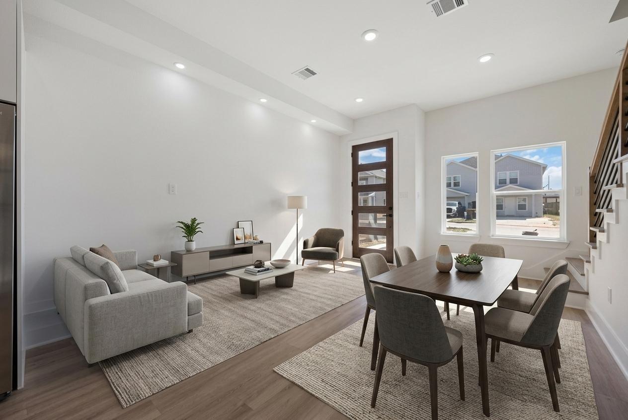 Open-plan living and dining room with gray seating, a dark dining table, and a glass-panel front door.