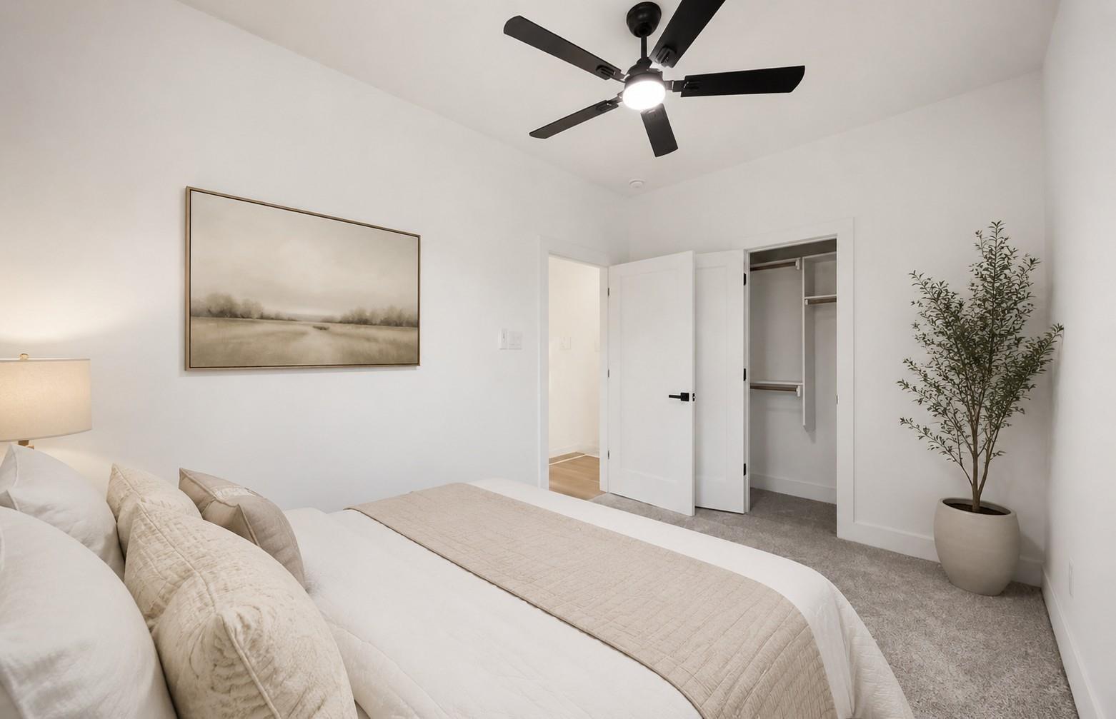 Staged bedroom with a black ceiling fan, neutral bedding, and an open closet.