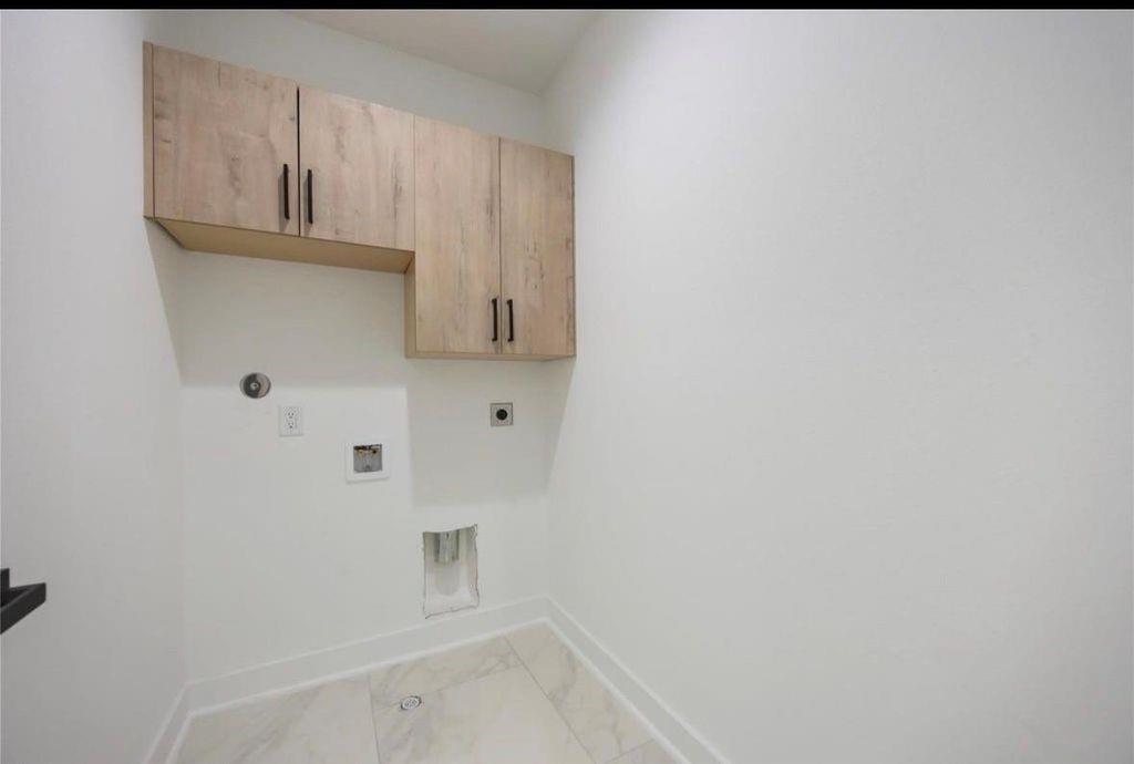 Laundry room with overhead wood cabinets, appliance hookups, and light tile flooring.