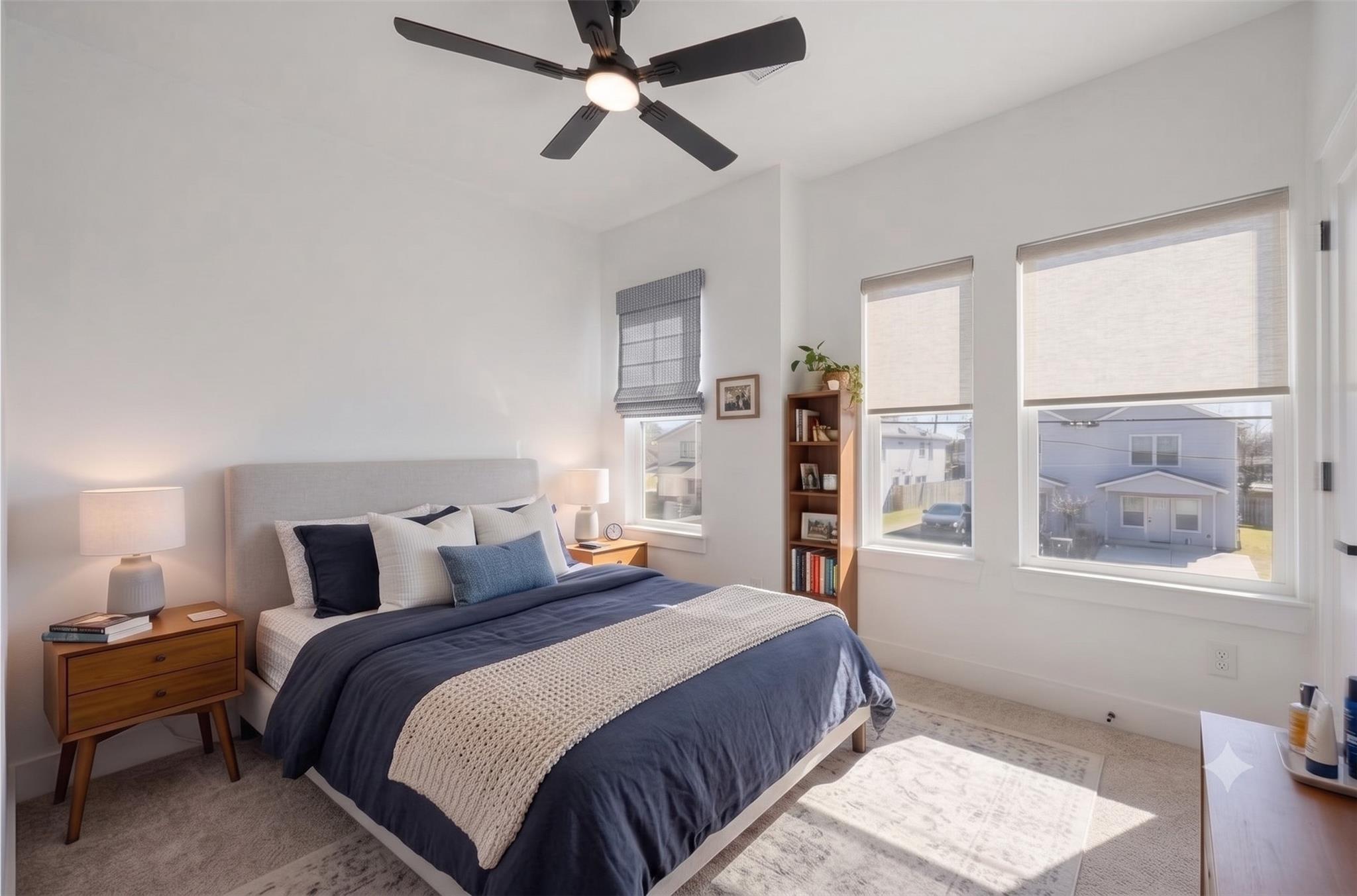 Bedroom with navy-and-white bedding, a black ceiling fan, and three shaded windows.