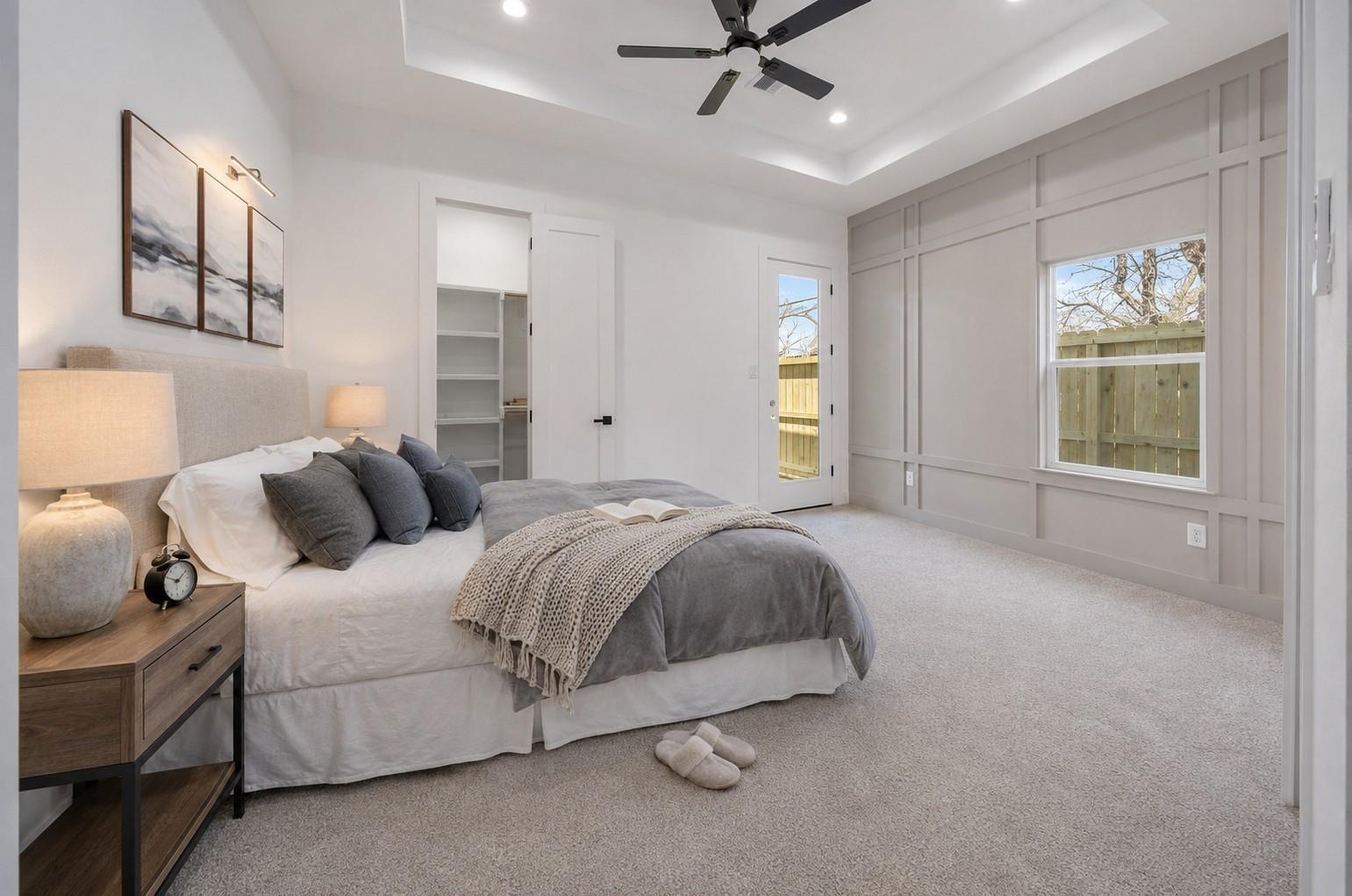 Staged bedroom with gray paneled walls, a ceiling fan, and a glass door to the fenced yard.
