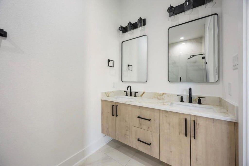 Bathroom with a light-wood double vanity, two sinks, black faucets, and matching rectangular mirrors.