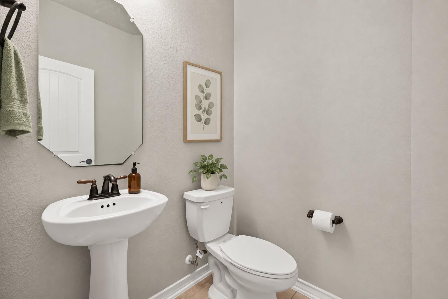 Bathroom with a pedestal sink, toilet, large mirror, and framed botanical print.
