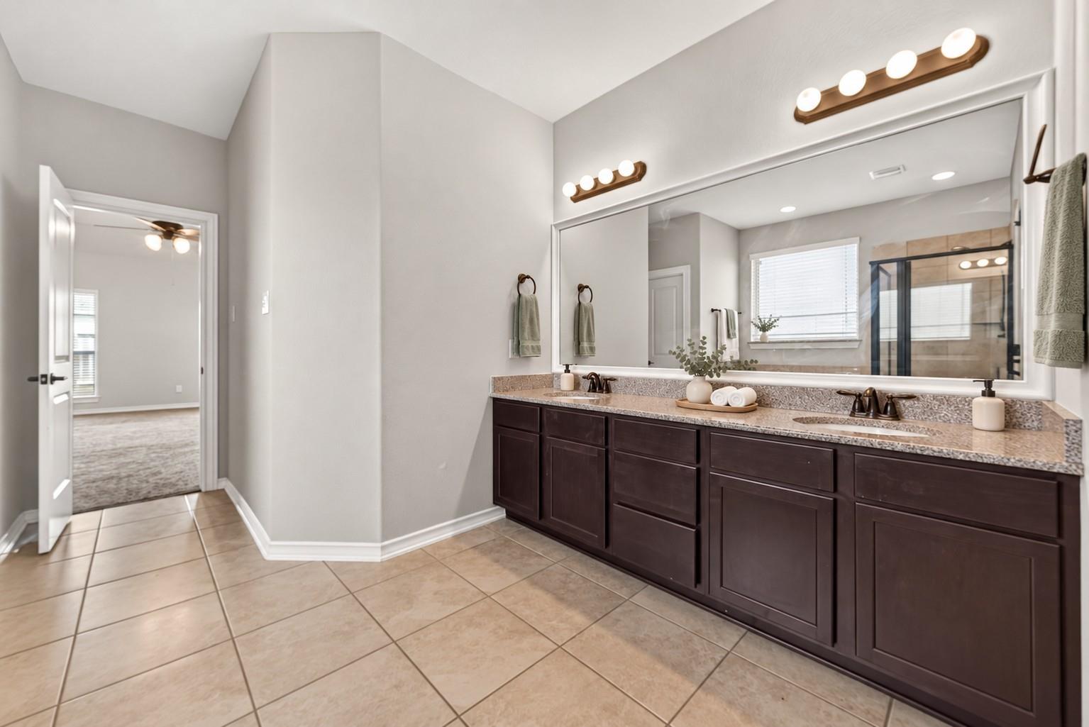 Bathroom with a long double vanity, dark wood cabinets, and a large mirror overlooking a glass shower.