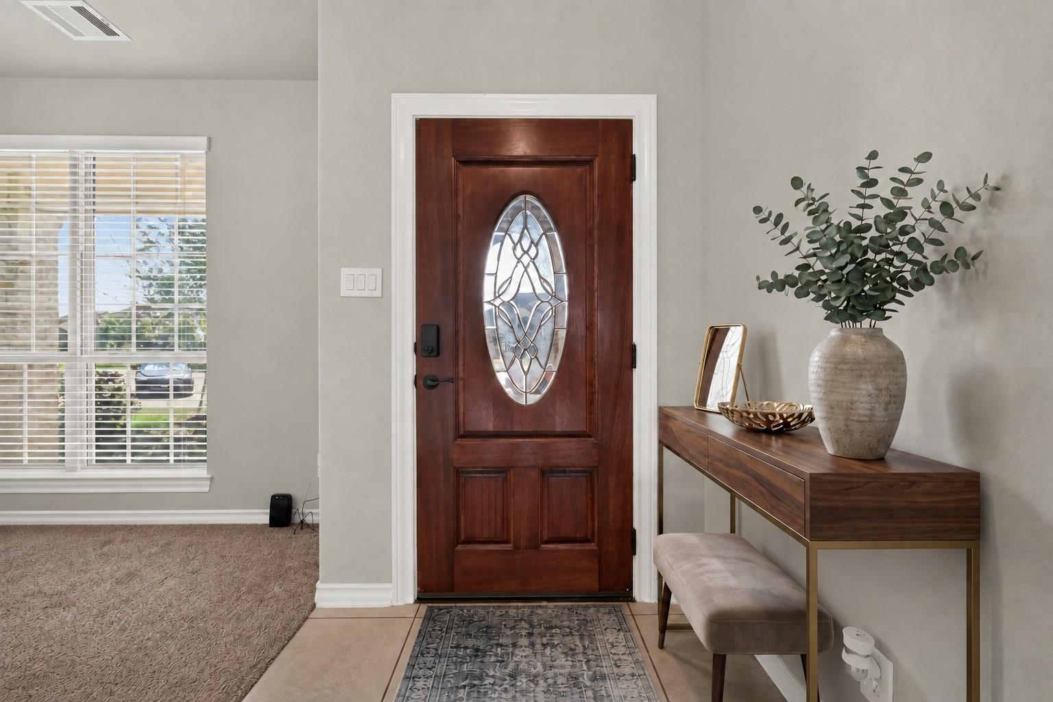Entryway with a dark wood front door featuring an oval decorative glass panel and a console table with greenery.