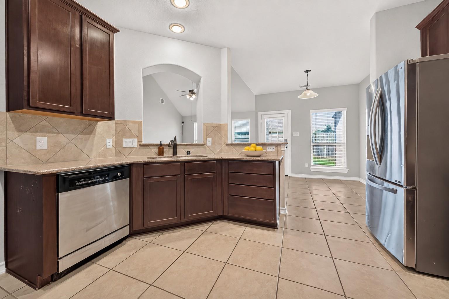 Kitchen with dark wood cabinets, beige tile surfaces, and stainless steel appliances opening to a dining area.