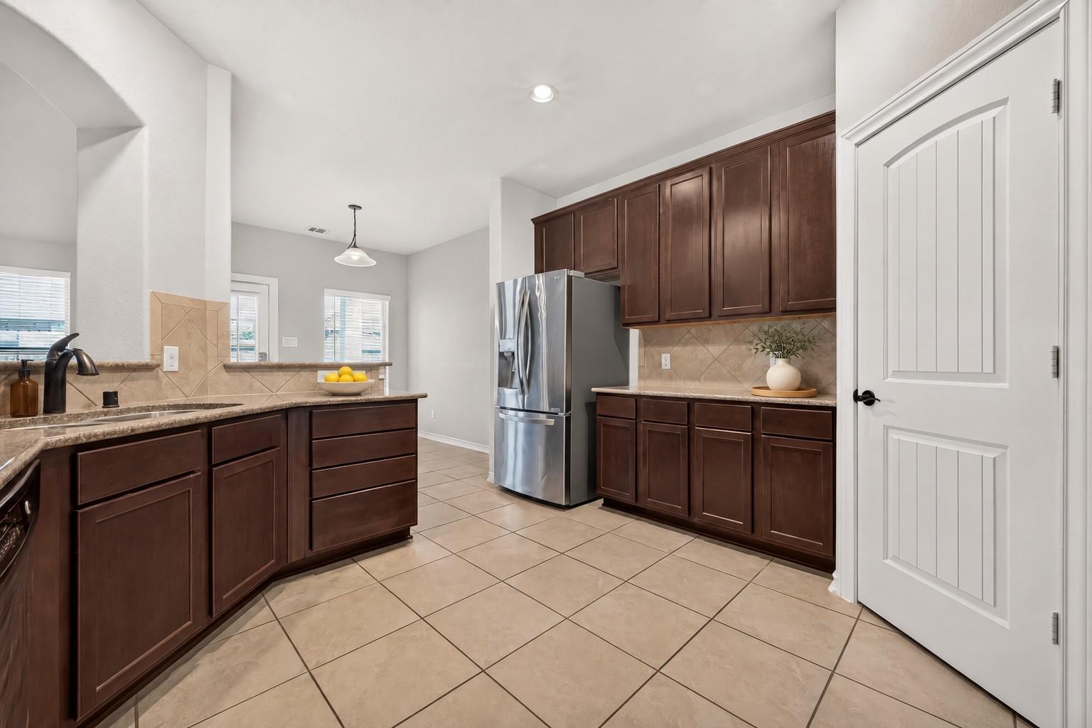 Kitchen with dark wood cabinets, granite counters, beige tile floors, and a stainless steel refrigerator.
