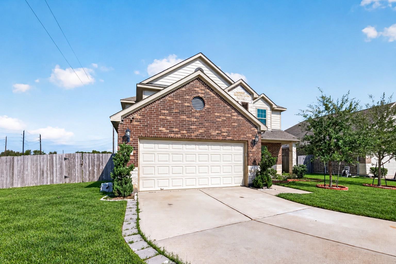 Two-story brick house with a white double garage, wide driveway, and fenced lawn.