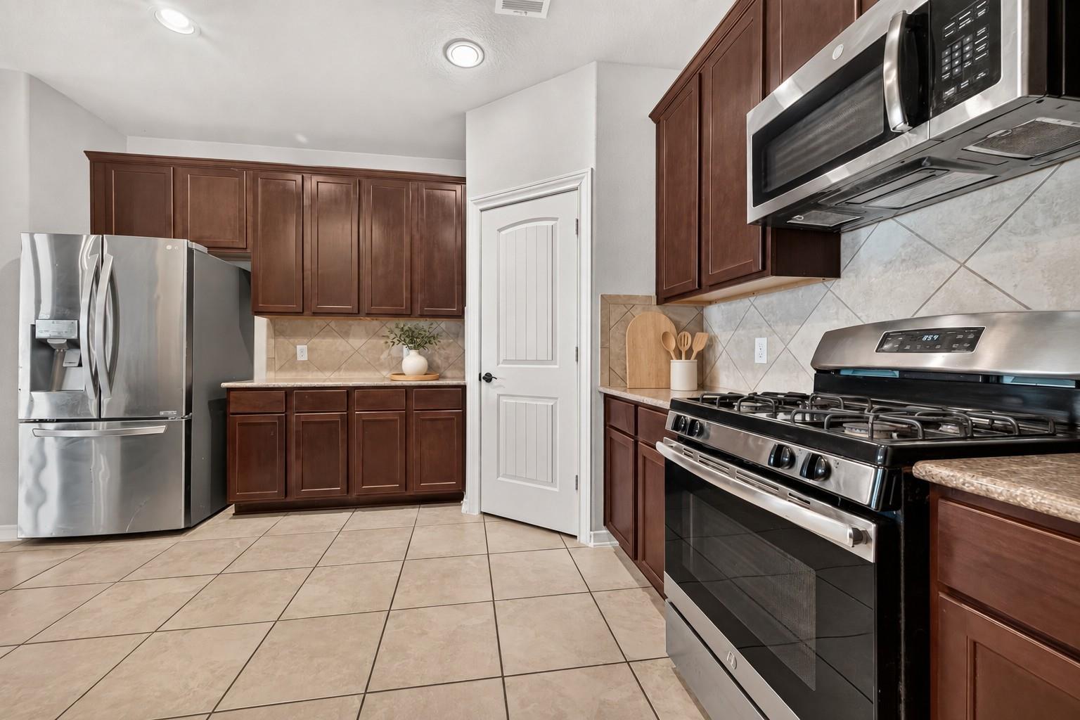 Kitchen with dark wood cabinetry, stainless steel appliances, and light tile floors.