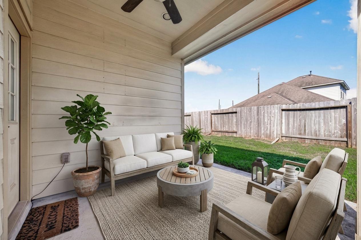 Covered patio with cushioned seating and potted plants overlooking a fenced backyard.