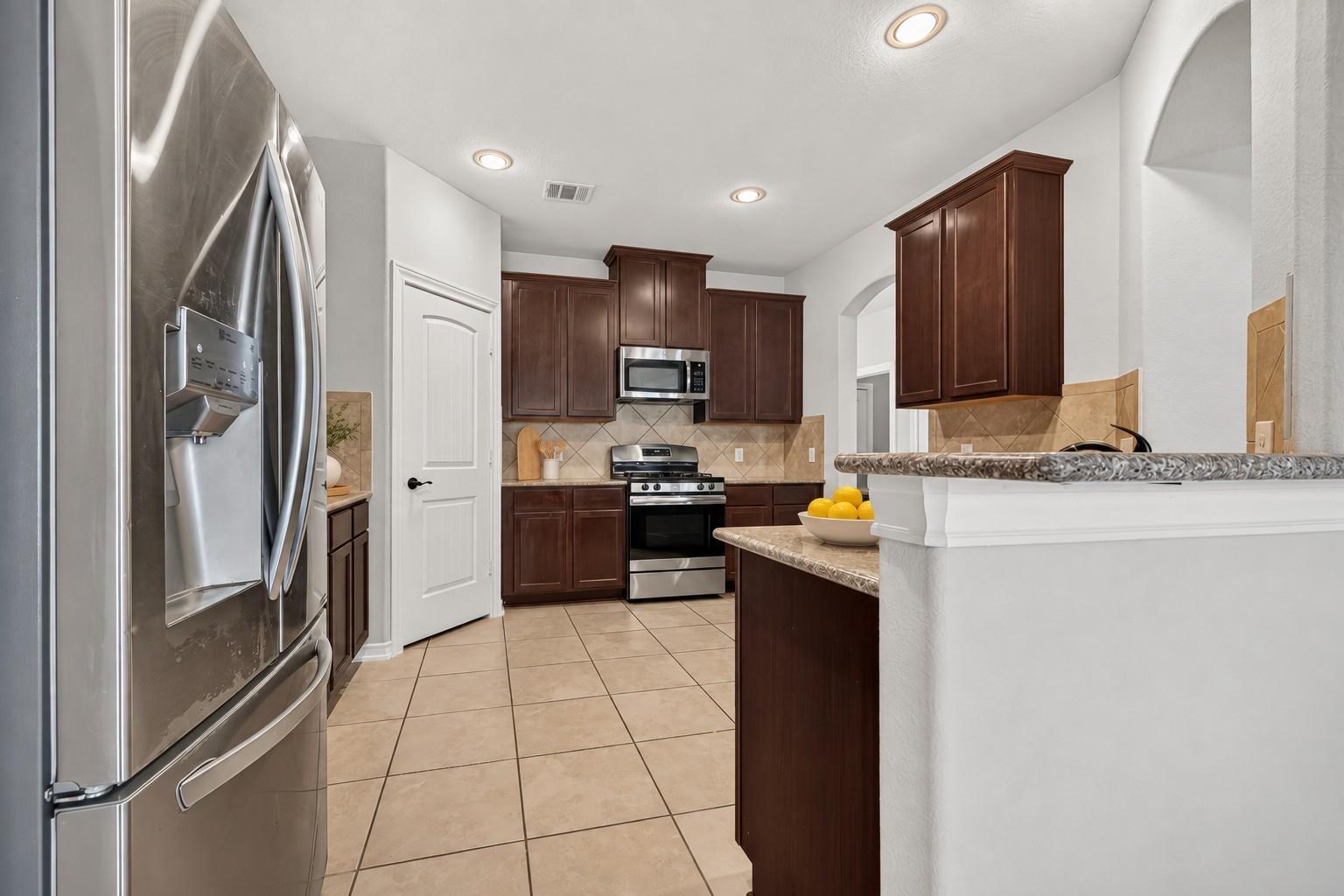 Kitchen with dark wood cabinets, stainless steel appliances, and a stone-counter peninsula.