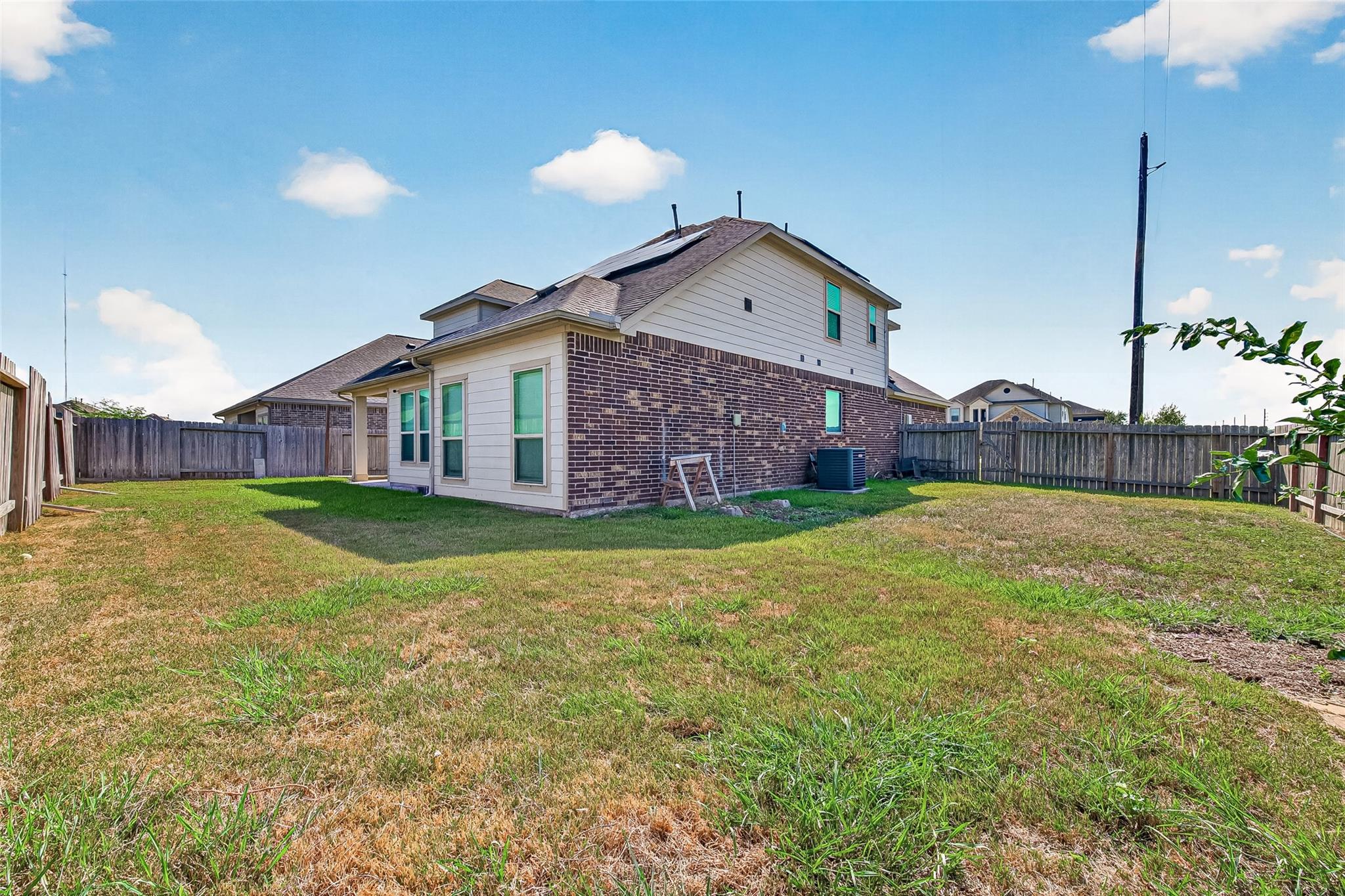 Rear exterior of a two-story brick house with a fenced backyard and patchy lawn.