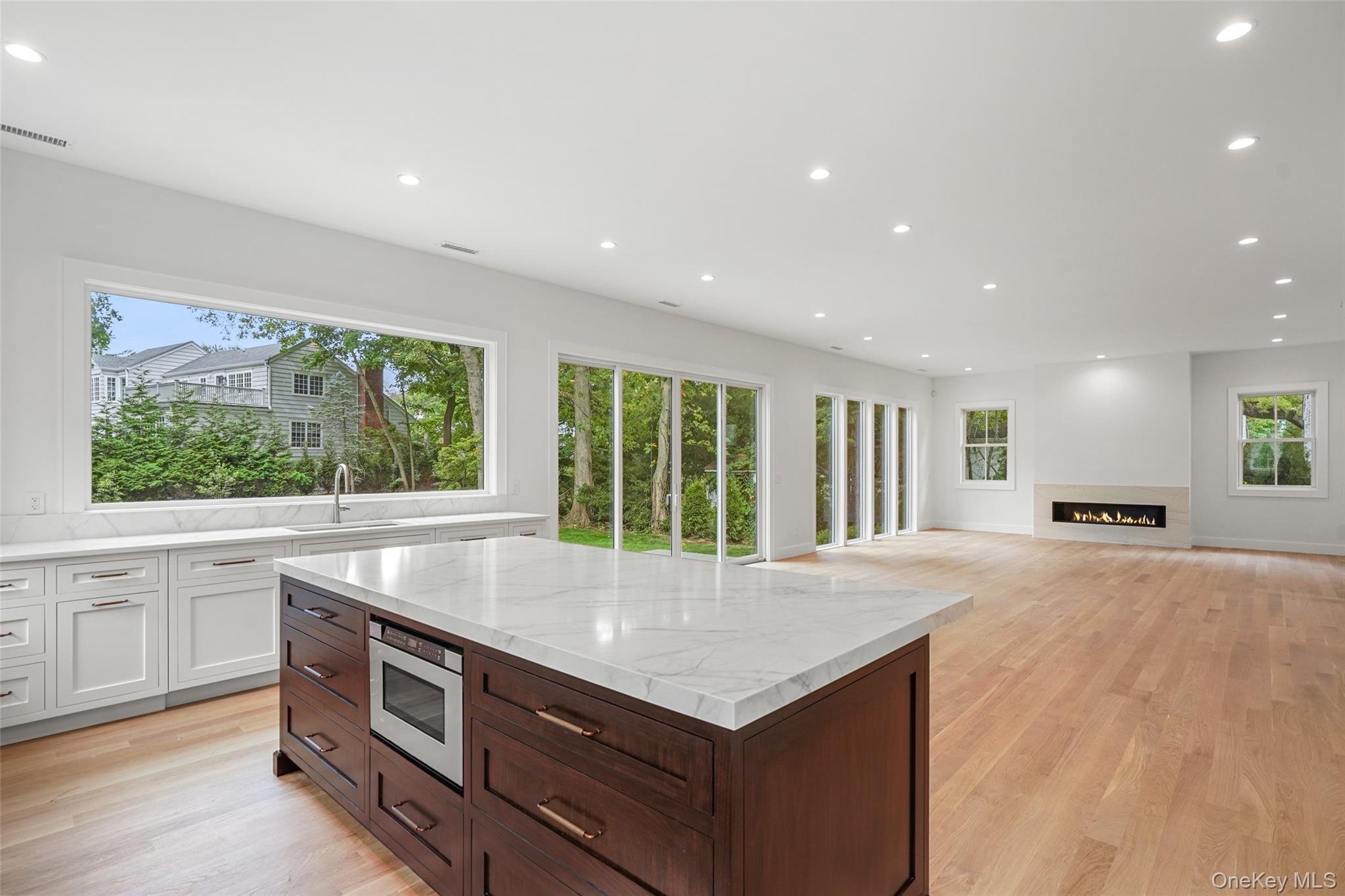Kitchen with a large marble island, dark wood cabinetry, expansive windows, and a linear fireplace.