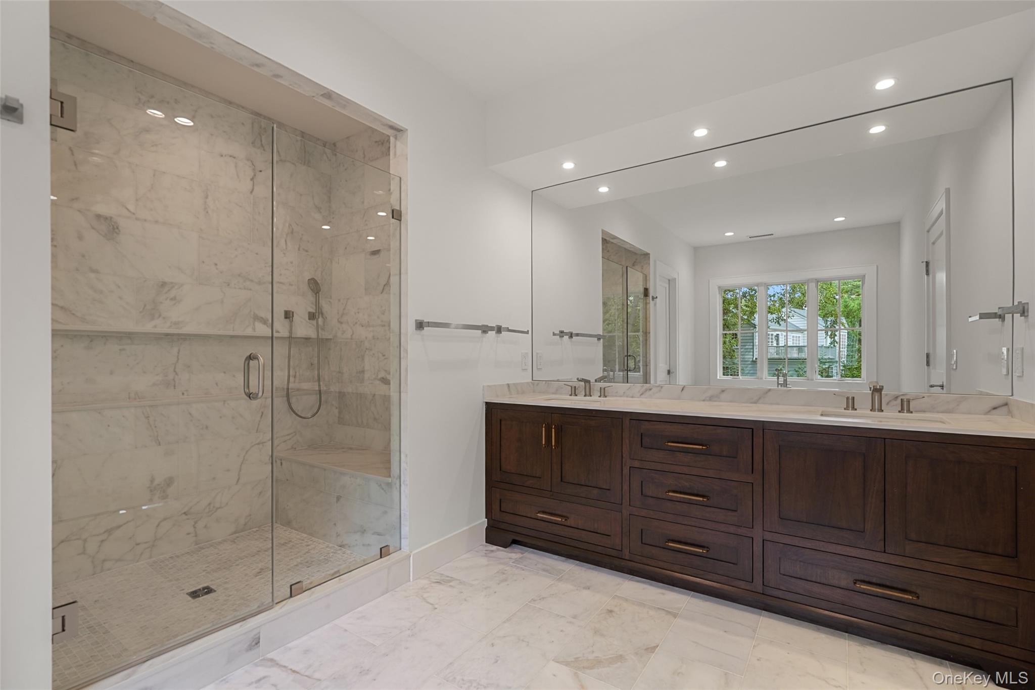 Bathroom with a glass-enclosed marble shower and dark wood double vanity.