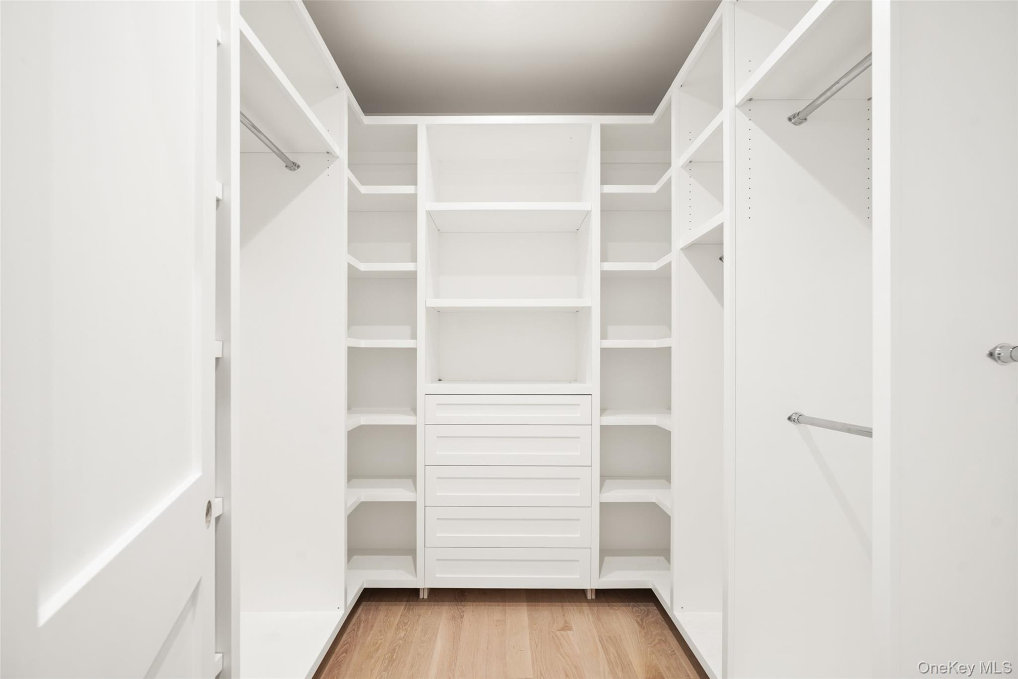 Walk-in closet with white built-in shelving, central drawers, and a light wood floor.