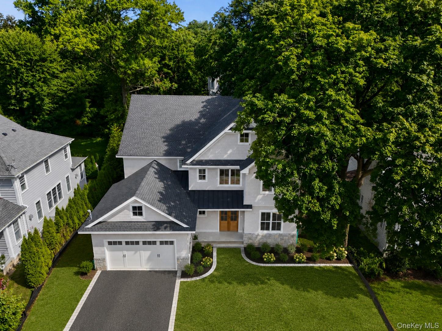 Aerial view of a gray two-story home with a two-car garage, landscaped lawn, and mature trees.