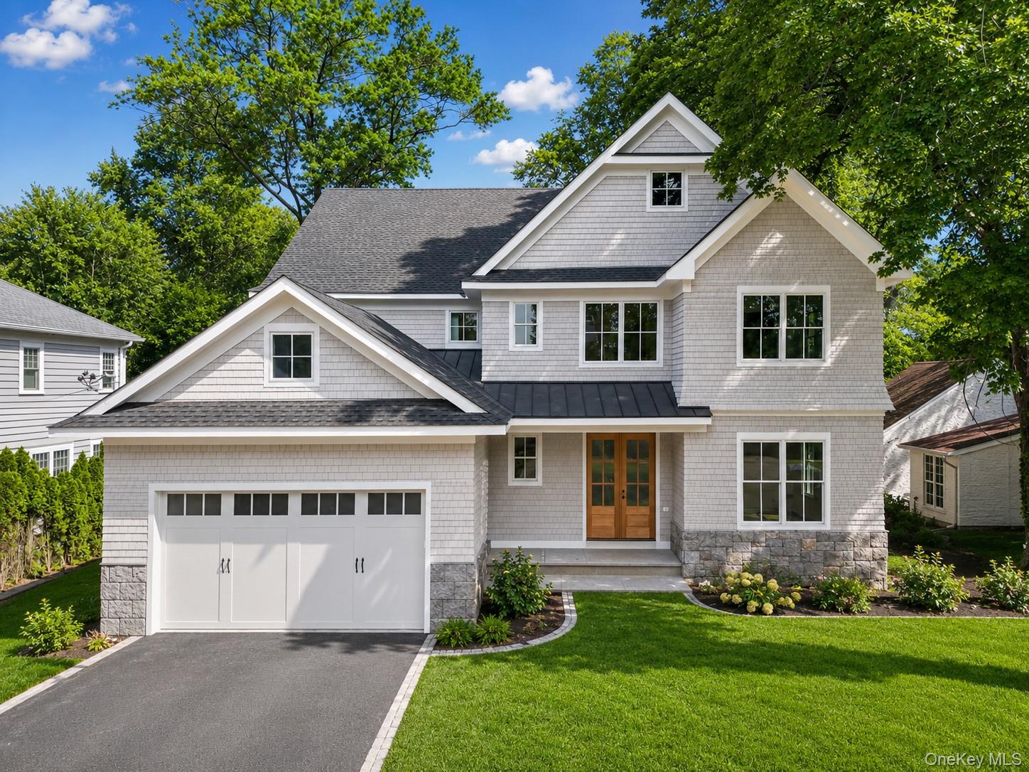 Gray shingle two-story house with a double garage, wooden front door, and landscaped lawn.