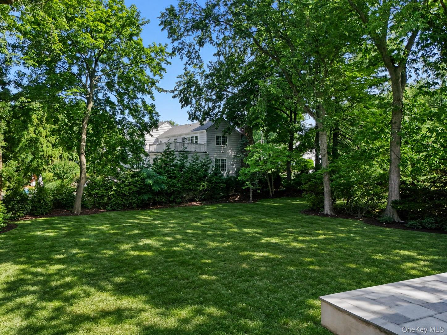 Gray two-story house with a balcony behind mature trees and a broad shaded lawn.
