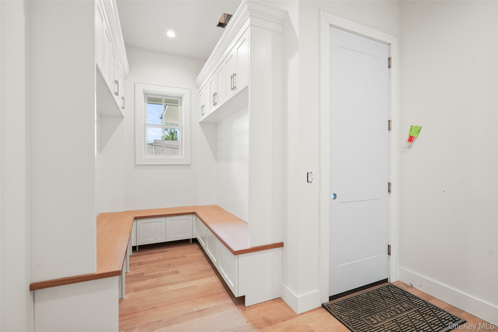 Mudroom with white built-in cabinets, a wood-topped bench, and a window.