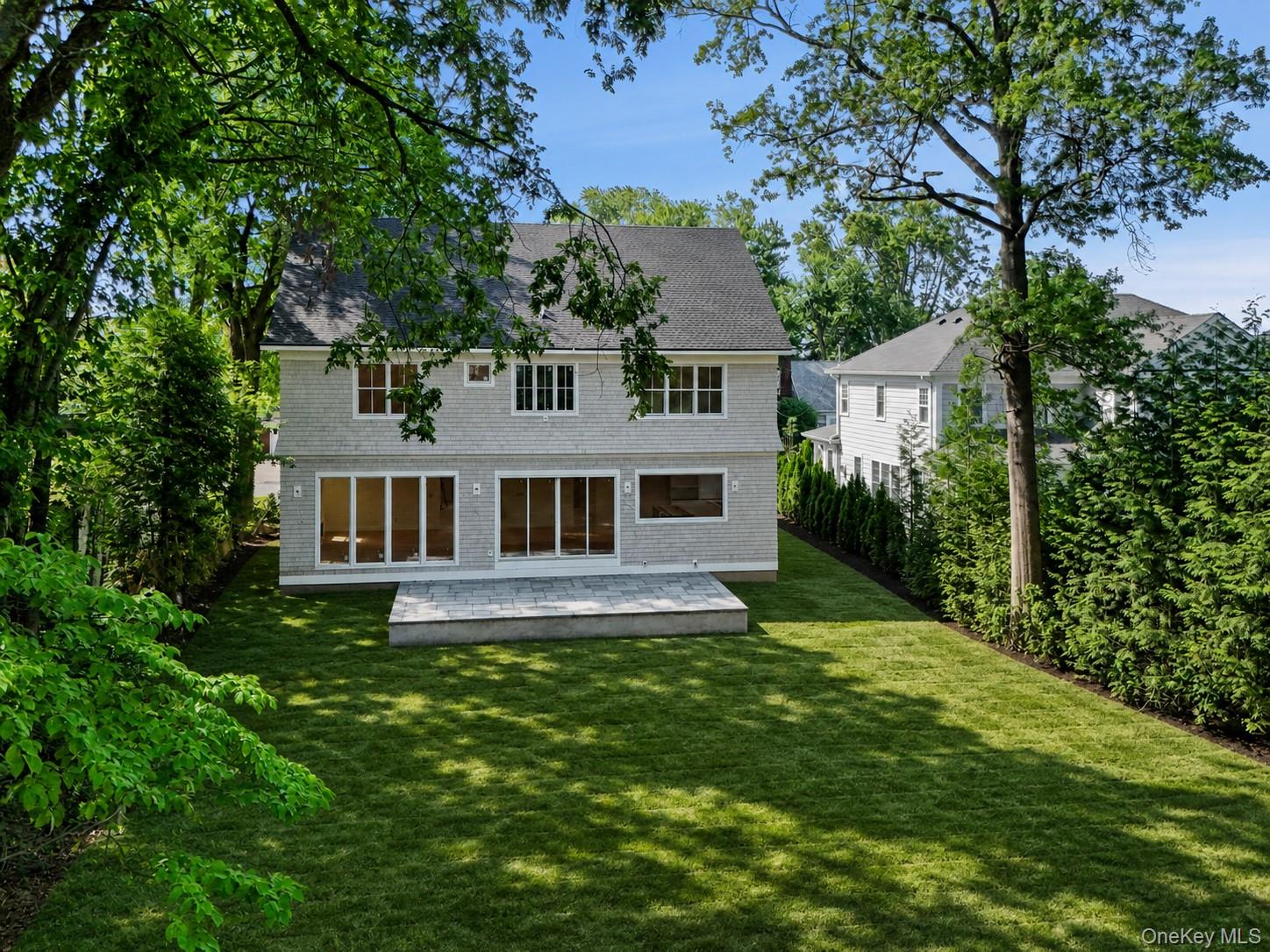 Two-story gray-shingled house behind a stone patio and leafy backyard.
