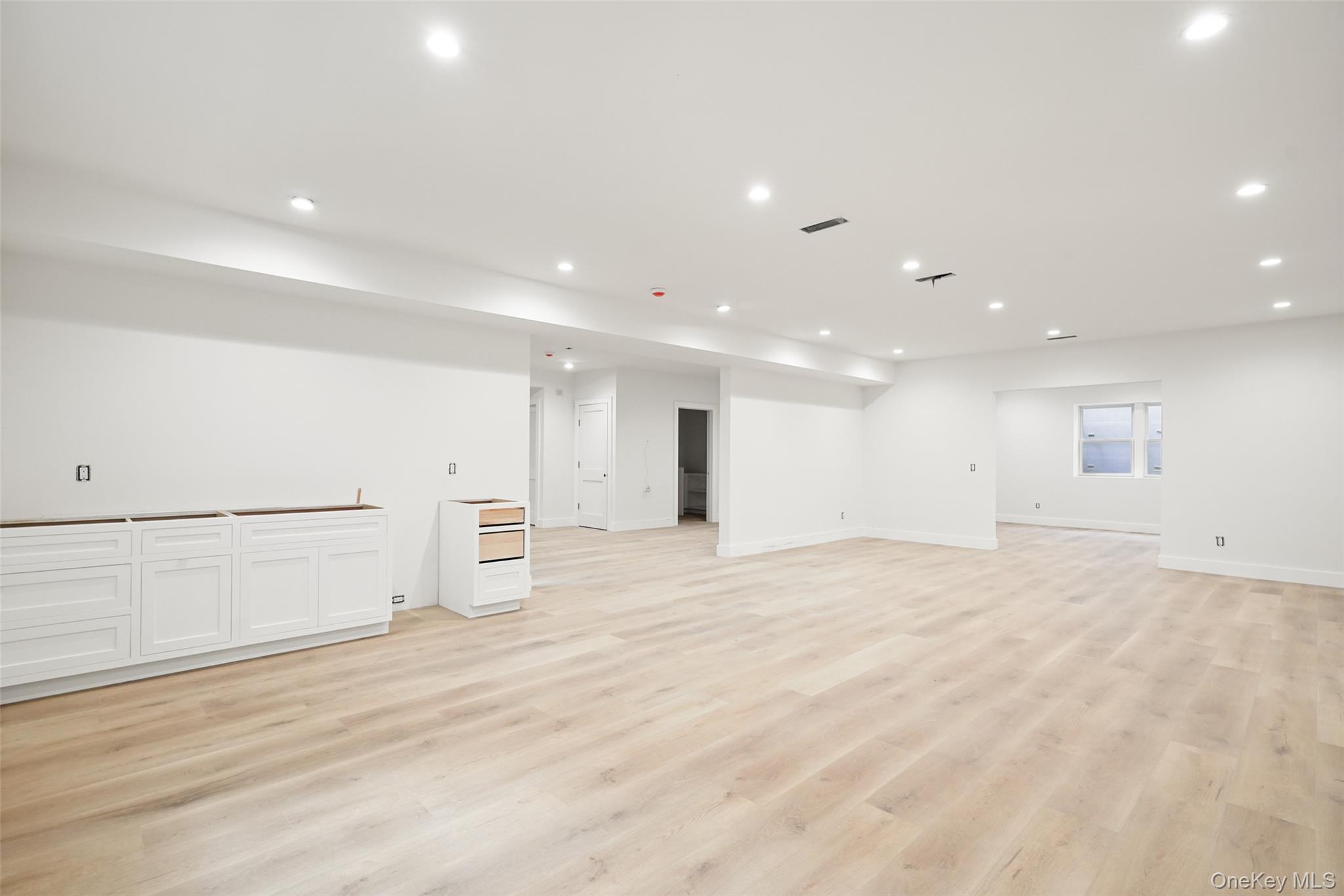 Large basement room with pale wood floors, recessed lights, and partially installed white cabinetry.