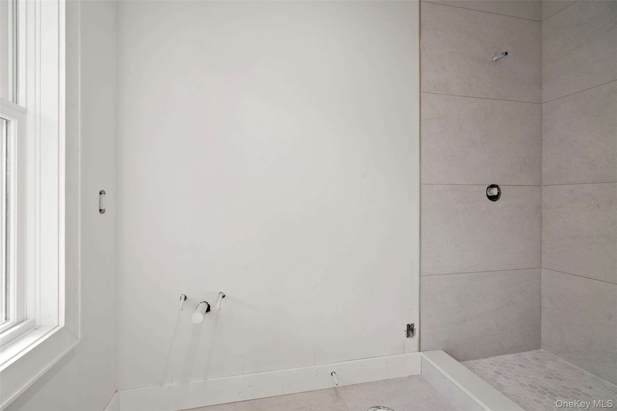 Unfinished bathroom with exposed plumbing, a tiled shower enclosure, and a window.