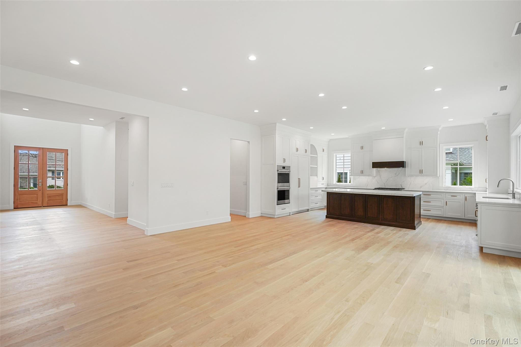 Open-plan kitchen with white cabinetry, marble counters, dark wood island, and pale hardwood floors.