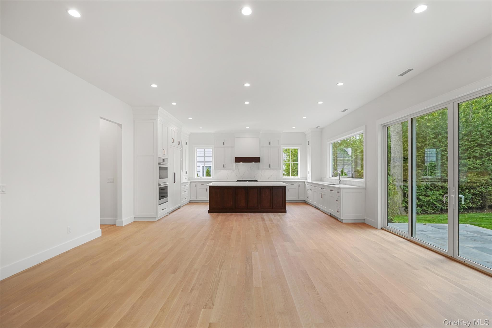 Modern white kitchen with a dark wood island, light wood floors, and sliding doors to a patio.