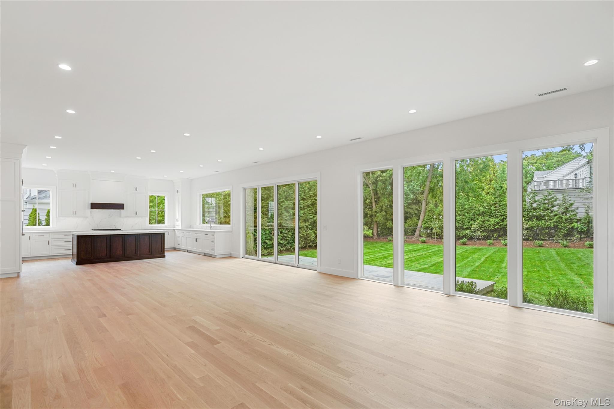 Vacant kitchen and living area with a dark island and large windows overlooking the lawn.