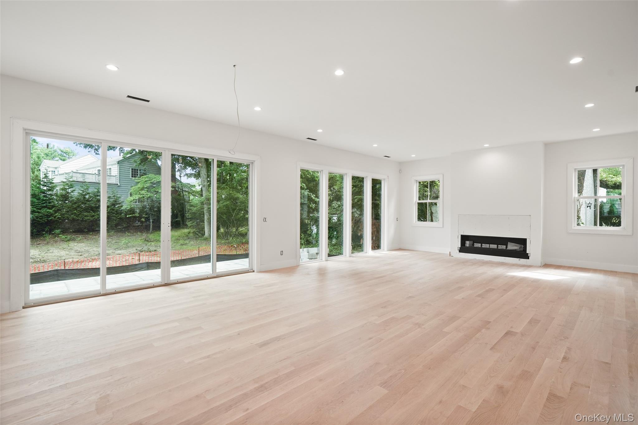Empty living room with pale wood floors, broad sliding glass doors, and a modern fireplace.