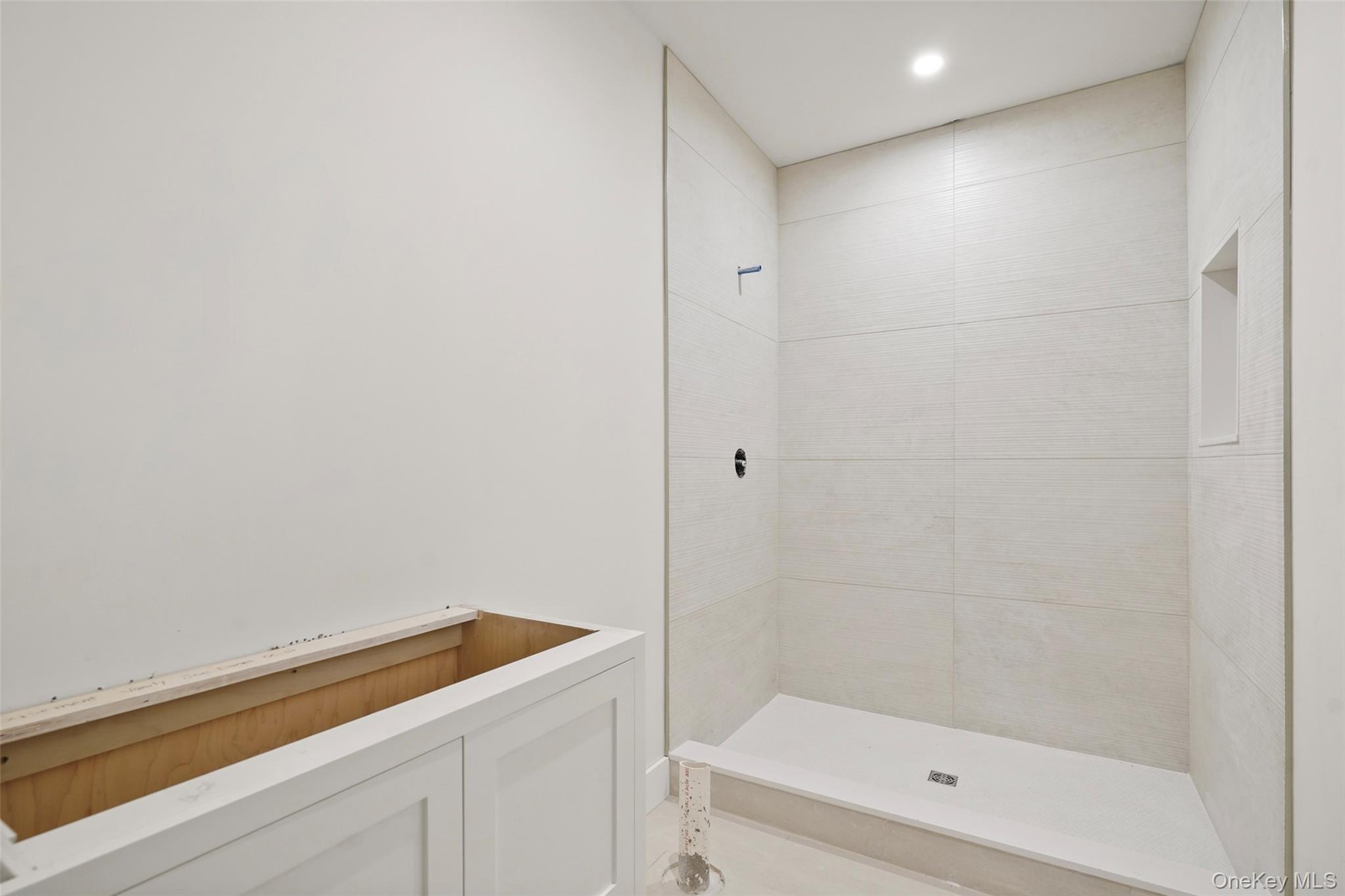 Bathroom under construction with a white-tiled walk-in shower and unfinished vanity.
