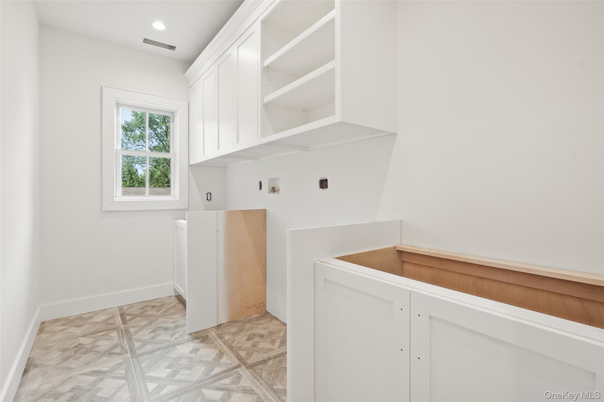 Bathroom under construction with white cabinetry, an unfinished vanity, patterned tile floor, and a window.