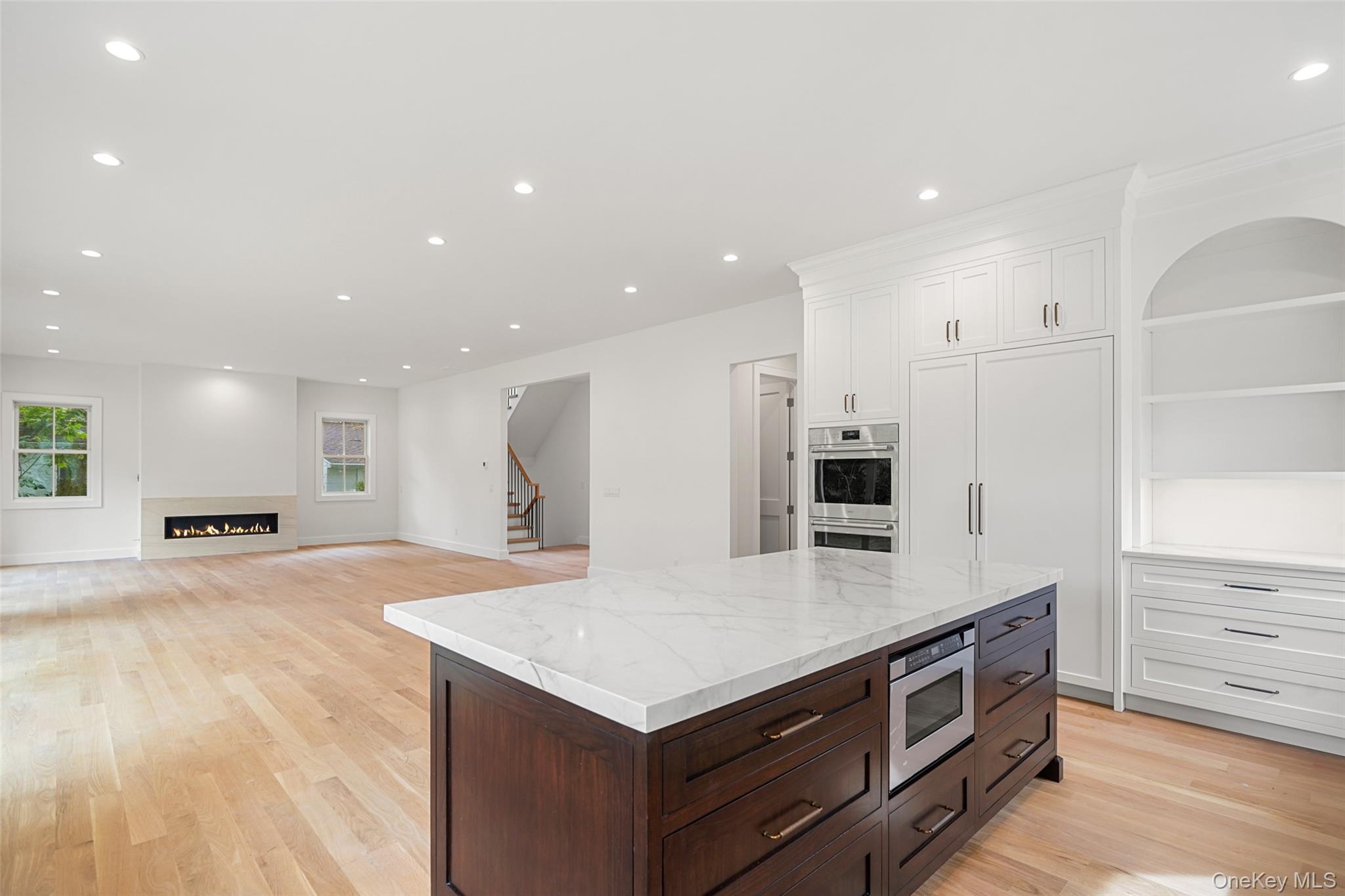 Open kitchen with a marble island, dark wood cabinetry, and a fireplace in the adjoining living area.
