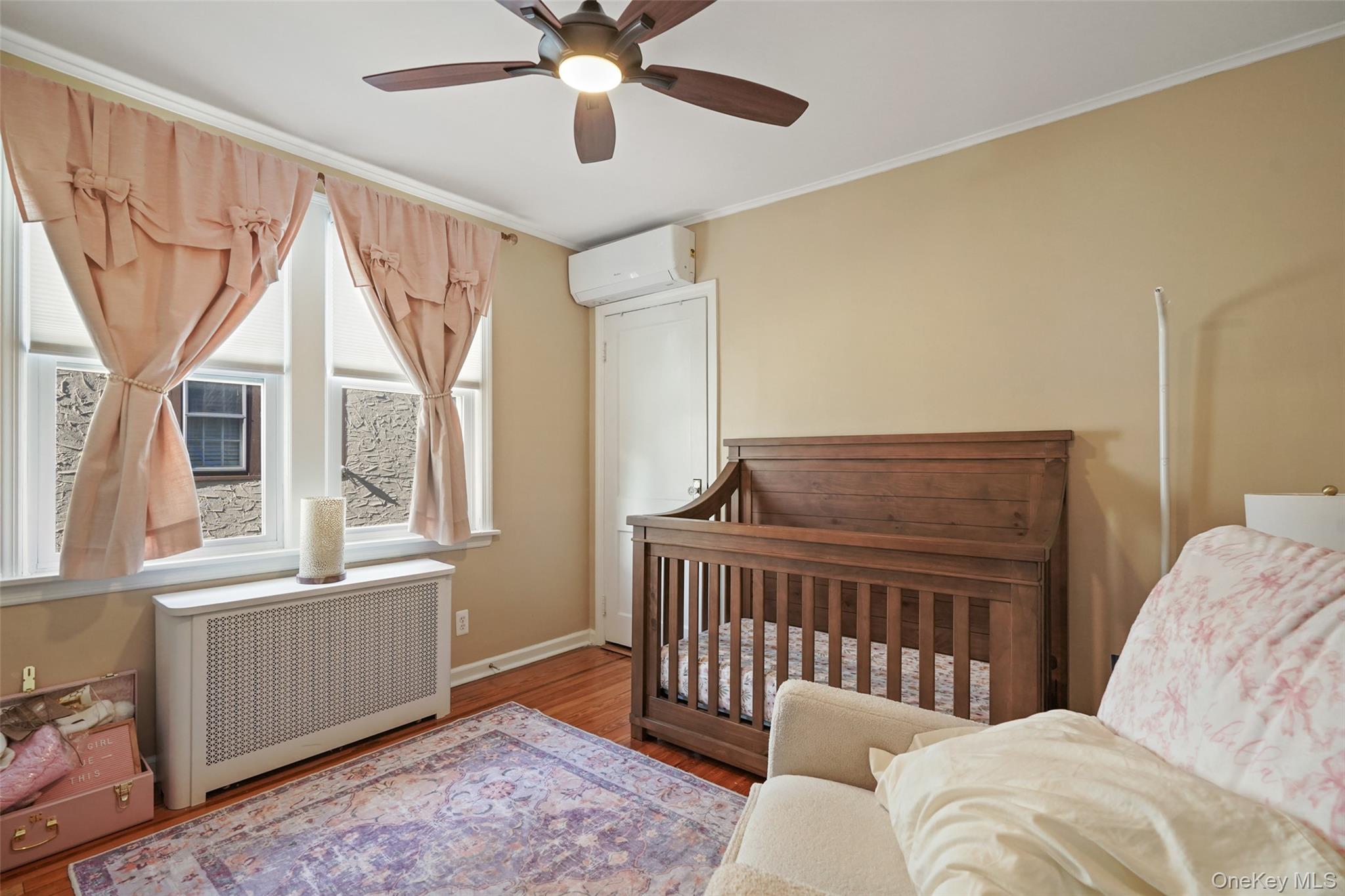 Nursery bedroom with a dark wood crib, pink curtains, and a ceiling fan.