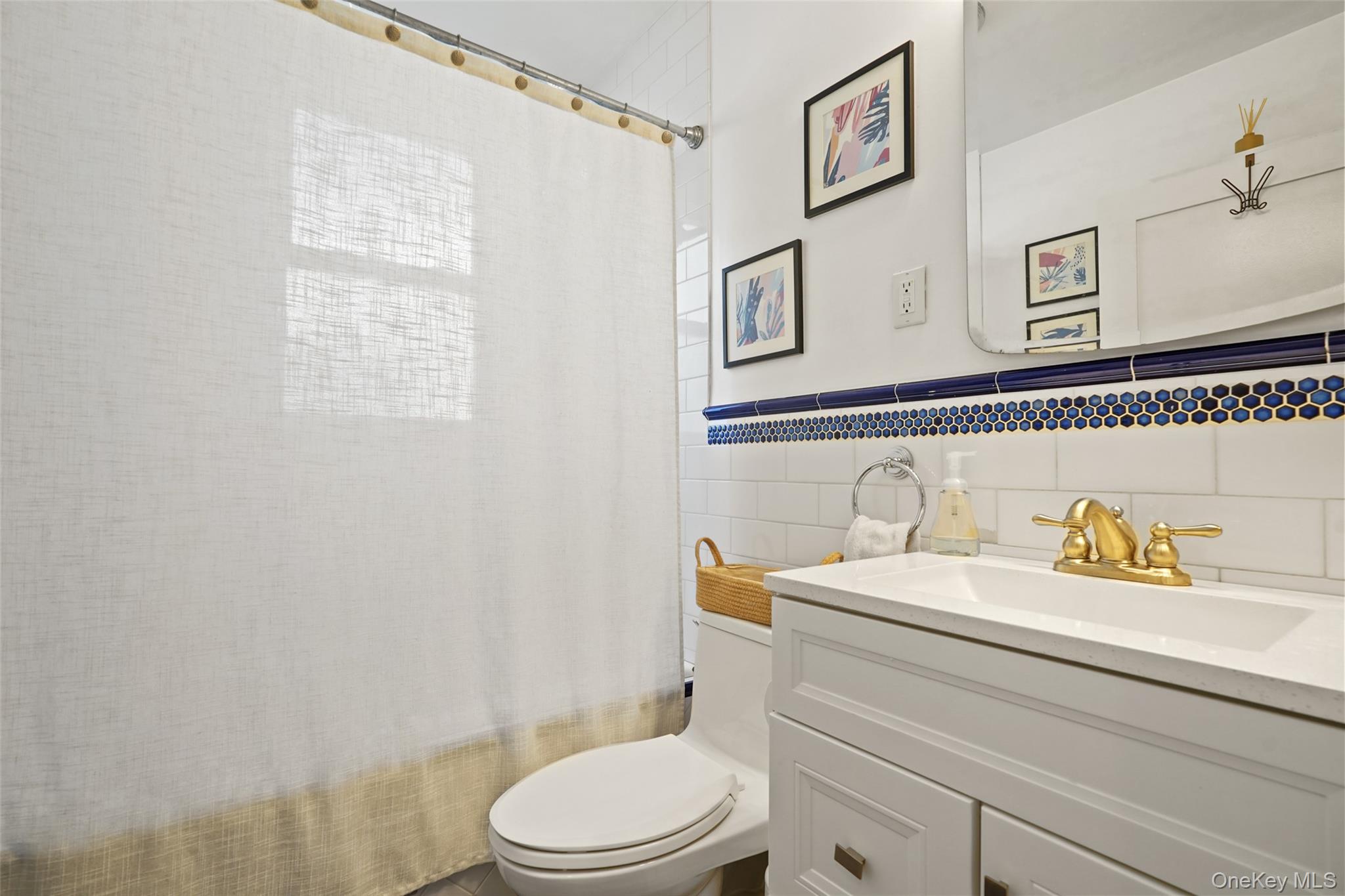 Bathroom with white vanity, gold faucet, and blue-and-gold tile border.