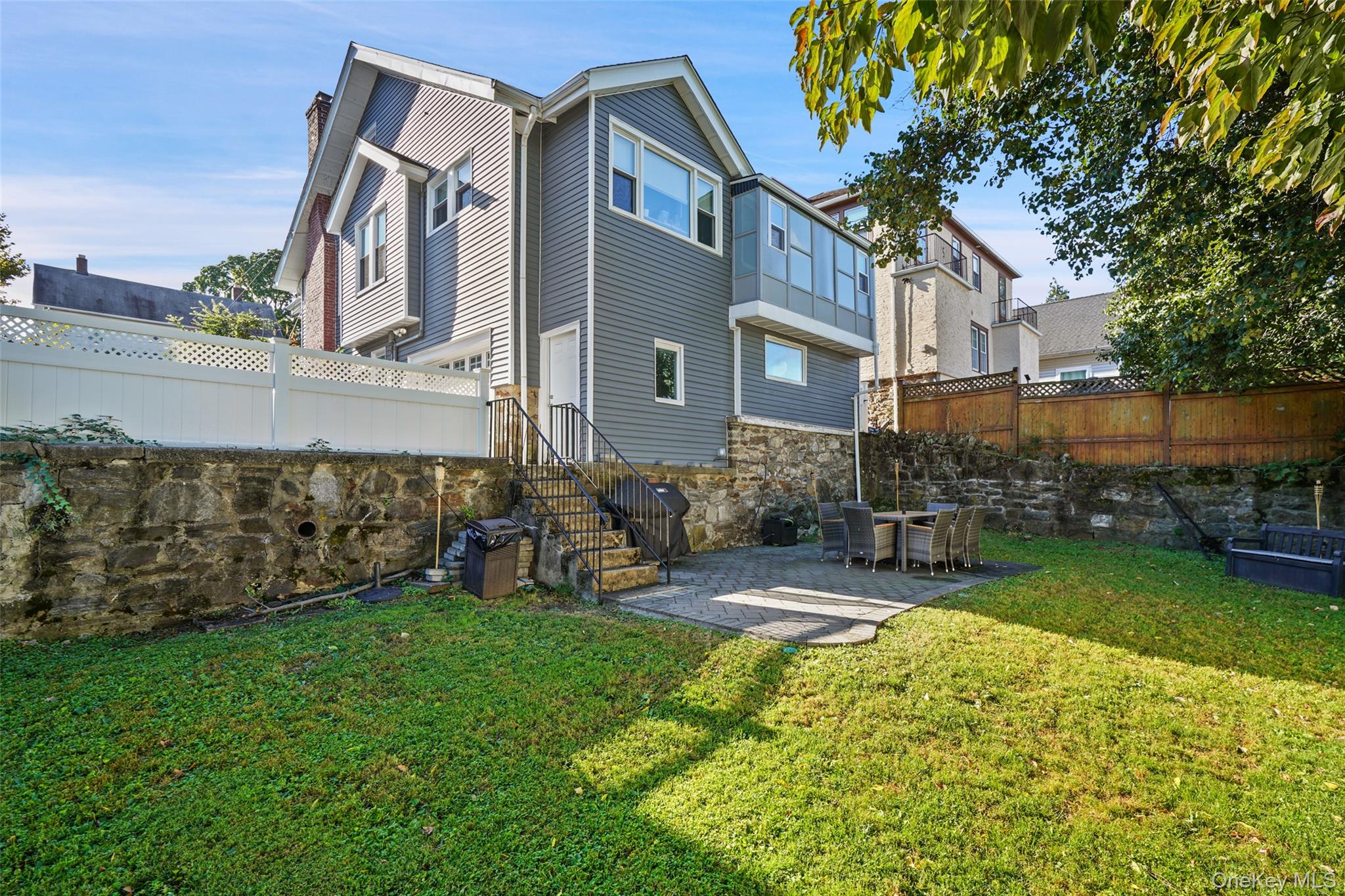 Gray-sided house behind a stone retaining wall, with a lawn and patio dining area.