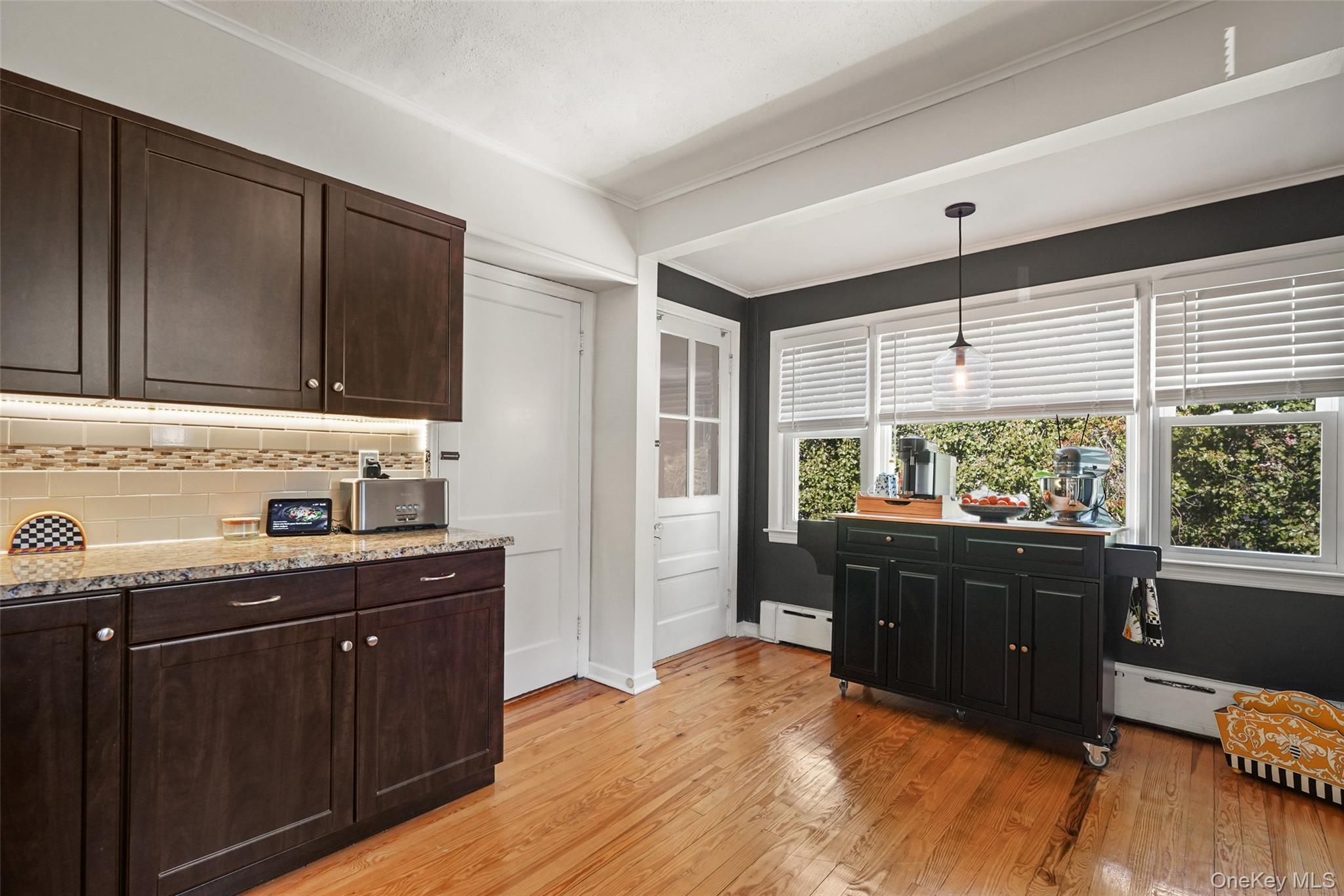 Kitchen with dark wood cabinets, a rolling island beneath wide windows, and polished hardwood floors.