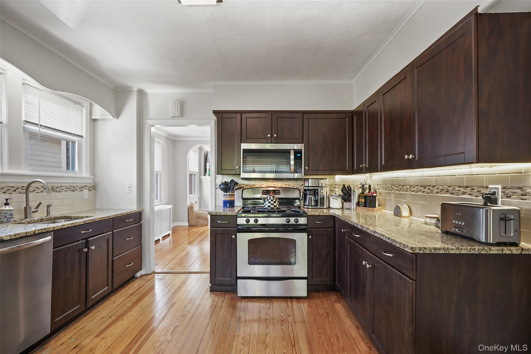 Kitchen with dark wood cabinets, granite counters, stainless steel appliances, and hardwood floors.